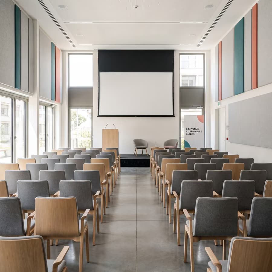 Colloque : salle claire, écran baissé et pupitre face aux rangées de chaises