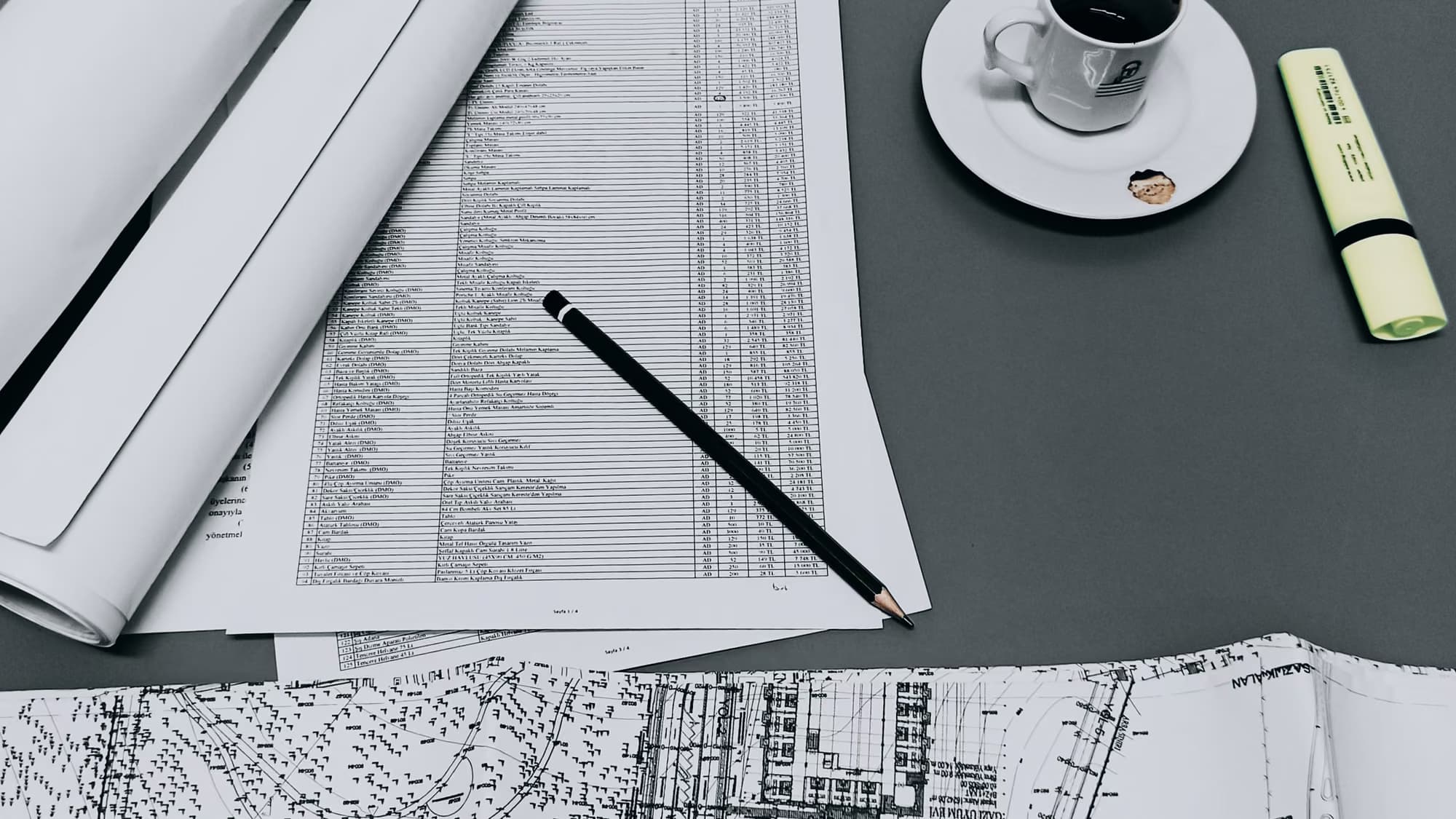 Plans roulés, crayon et tasse posés sur une table de travail